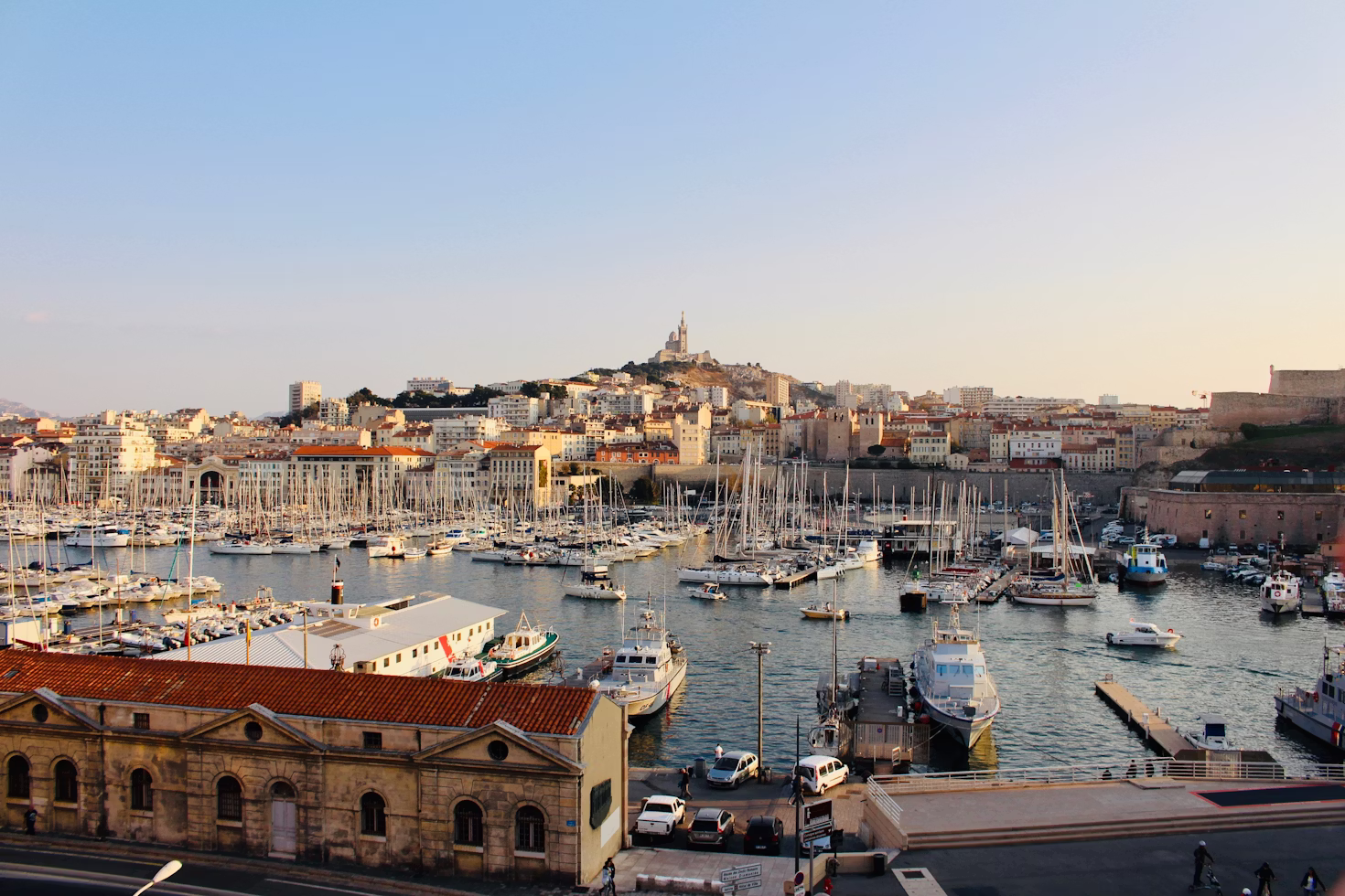 Vue panoramique sur le Vieux-Port de Marseille avec ses bateaux au coucher du soleil et Notre-Dame de la Garde en arrière-plan